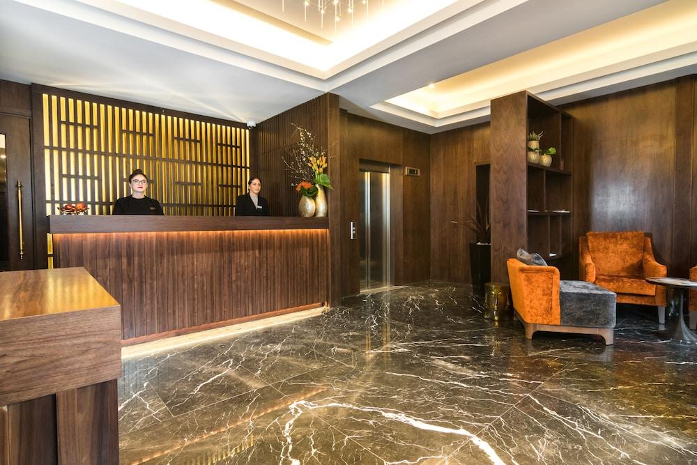 Montcalm Chilworth Townhouse, Paddington Hotel London Ngoại thất bức ảnh The photo depicts a modern hotel lobby. In the foreground, there is a reception desk made of dark wood, behind which two staff members are standing. The walls are adorned with a wooden panel design and there are decorative plants and flowers on the d