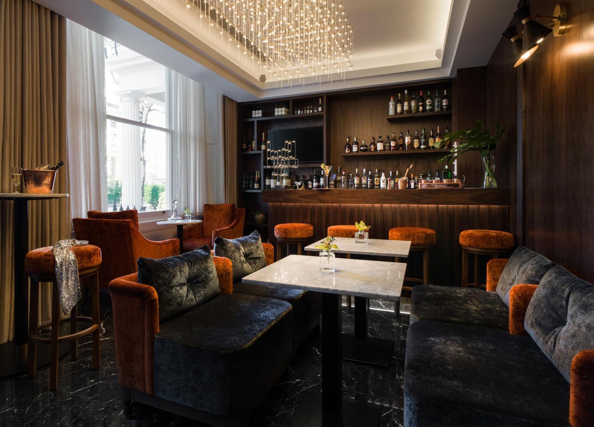 Montcalm Chilworth Townhouse, Paddington Hotel London Ngoại thất bức ảnh The photo shows a stylish interior of a bar or lounge area. There are plush seating arrangements with dark, velvet sofas and orange-accented chairs. The tables are marble-topped, and there are decorative elements such as a chandelier hanging from the