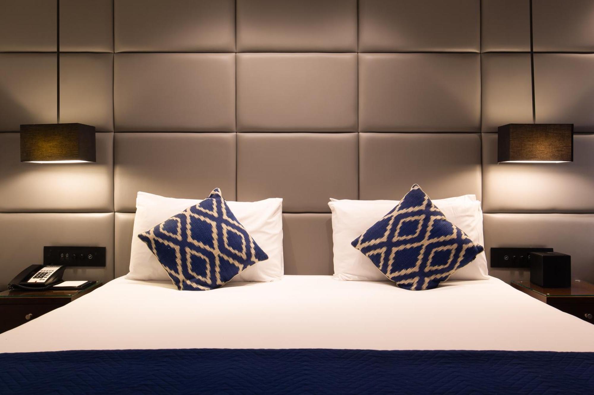 Montcalm Chilworth Townhouse, Paddington Hotel London Ngoại thất bức ảnh The photo shows a well-designed hotel room with a neatly made bed. The bed has a white duvet and two decorative pillows with a blue geometric pattern. The headboard is upholstered and features a grid-like design in neutral tones. On either side of th