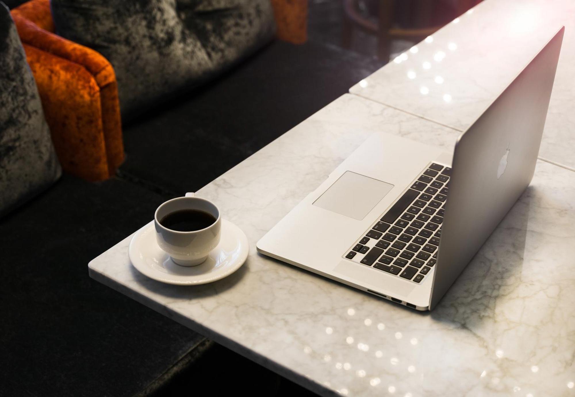 Montcalm Chilworth Townhouse, Paddington Hotel London Ngoại thất bức ảnh The photo shows a marble table with a laptop positioned on one side. Next to the laptop, there is a small cup of black coffee placed on a saucer. The background features a cozy seating area, with some upholstered chairs that have vibrant orange and d