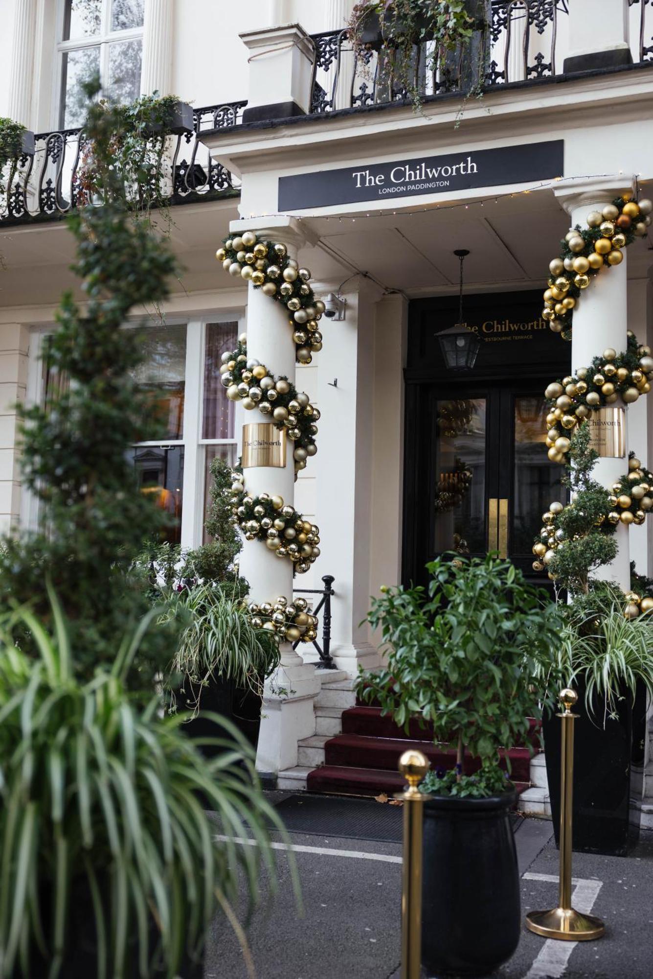 Montcalm Chilworth Townhouse, Paddington Hotel London Ngoại thất bức ảnh The photo shows an elegant entrance to a building, decorated with festive adornments. There are two tall columns wrapped in garlands made up of gold and black ornaments, giving a luxurious appearance. On either side of the entrance, there are potted 