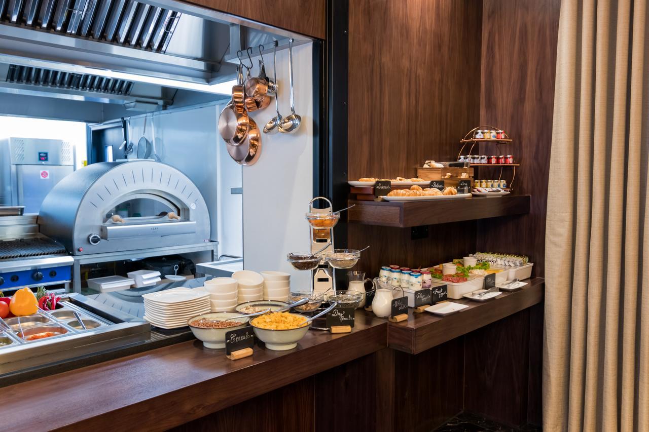 Montcalm Chilworth Townhouse, Paddington Hotel London Ngoại thất bức ảnh The photo shows a buffet area in a dining setting. There's a wooden counter displaying a variety of food items. On the left side, there are bowls containing different types of food, possibly salads or sides. On a tiered stand, there are desserts or s